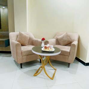 A room with a beige sofa set, a small round table with a white base, and a vase with a red flower.