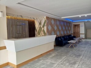 A reception area with a white counter, patterned wall, and blue seating.