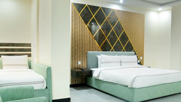 A hotel room with two beds, a nightstand, a small table with a vase, and a decorative wall panel. - Legend Hotel Kalam (Swat)