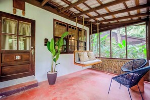 A room with a swing chair, a potted plant, and a view of greenery outside. - Sweet Songs Jungle Lodge (San Ignacio)