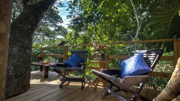 An outdoor deck with wooden furniture and a table, surrounded by lush greenery.