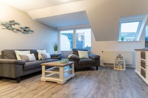 Ein modernes Wohnzimmer mit zwei Sofas, einem Couchtisch und Blick auf Gebäude durch große Fenster.