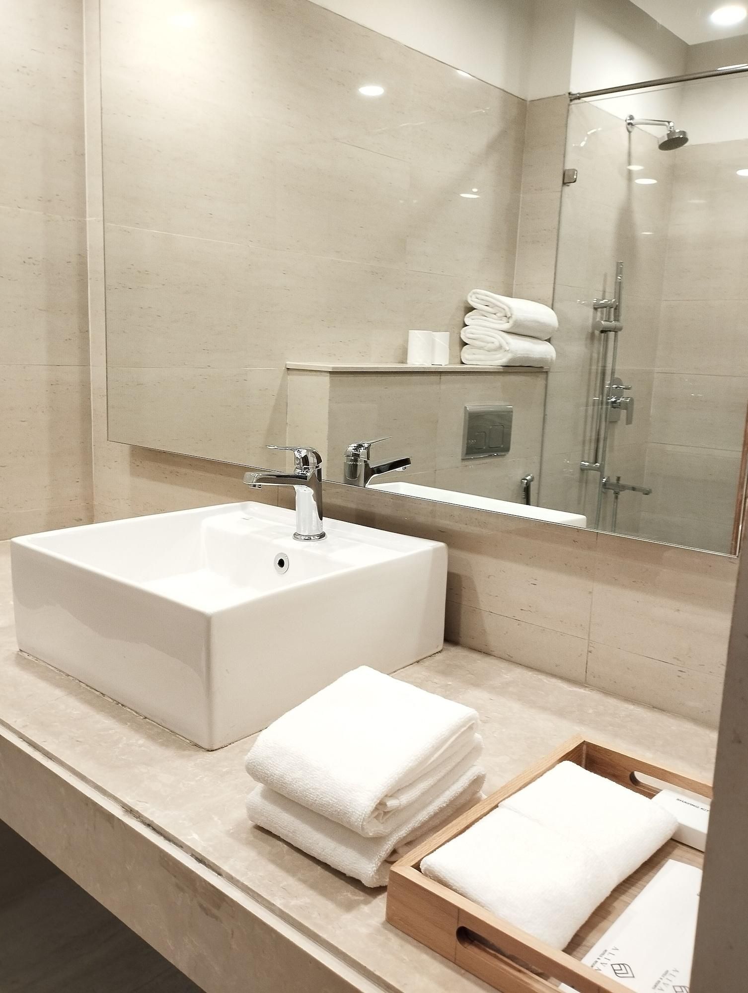 A modern bathroom with a large white sink, a glass shower enclosure, and neatly folded white towels on the counter.
