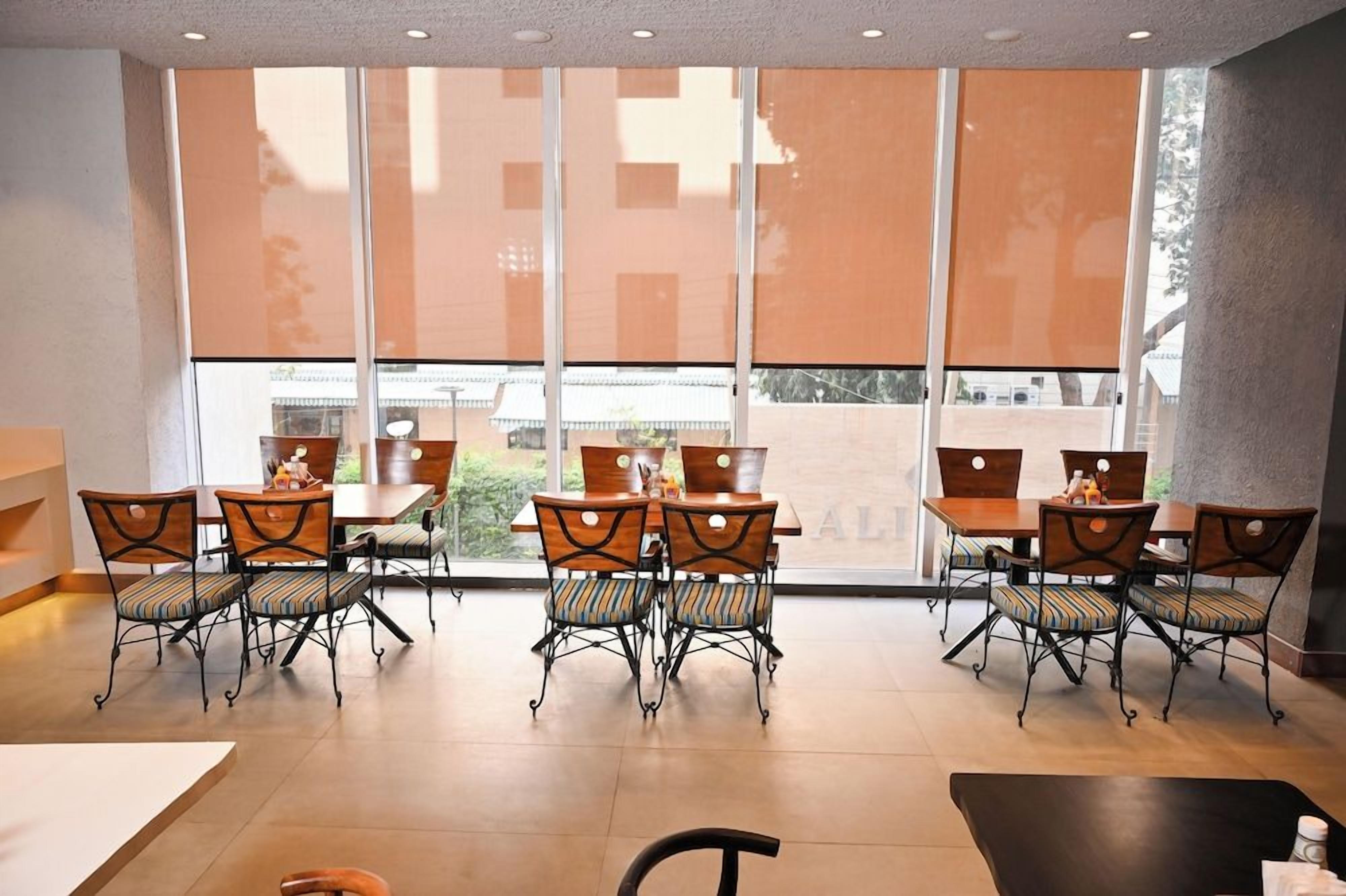 A dining area with tables and chairs, large windows, and a view of the outside.