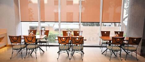 A dining area with tables and chairs, large windows, and a view of the outside.