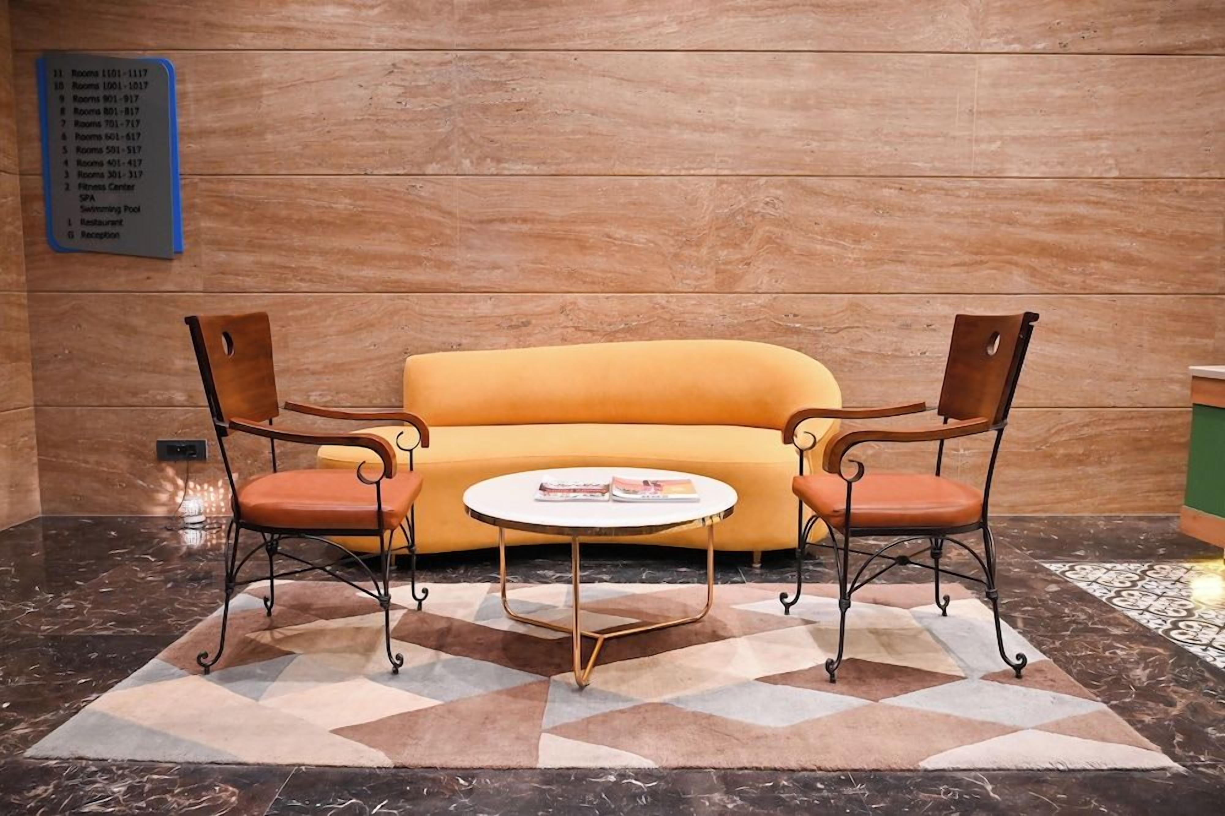 A lobby with a yellow sofa, two armchairs, a small round table, and a sign listing room numbers and amenities.