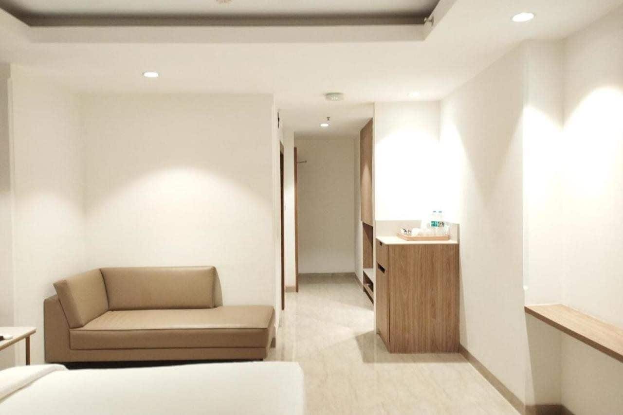 A hotel room with a sofa, a bed, a wooden cabinet, and a small table.