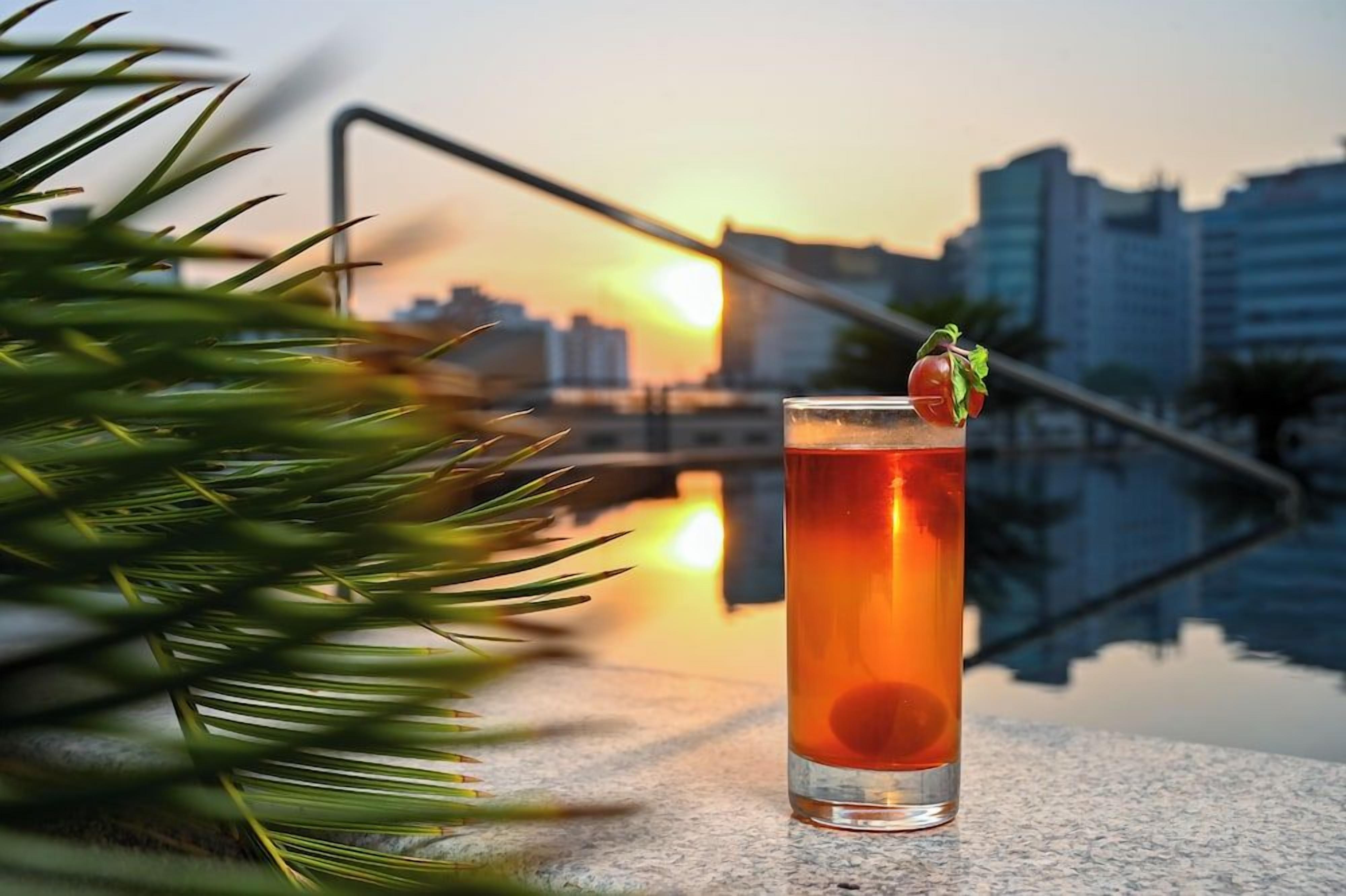 A tall glass with a beverage, a garnish, and a cityscape in the background.