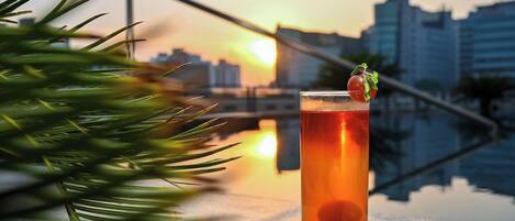 A tall glass with a beverage, a garnish, and a cityscape in the background.
