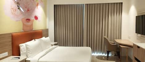 A hotel room with a bed, a desk, a chair, a TV, and a large floral mural on the wall.