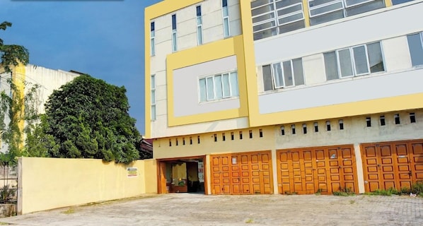 A multi-story building with a yellow facade, a large tree in front, and a gated entrance. - Super OYO 93930 The Sunny Inn (Medan)