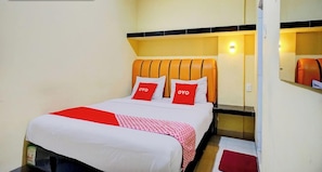 A hotel room with a bed, two pillows with 'OYO' branding, a red and white patterned throw, and a red rug. - Super OYO 93930 The Sunny Inn (Medan)