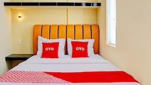A hotel room with a bed, two pillows with the word 'OYO' on them, a red and white patterned bedspread, and a window on the right side. - Super OYO 93930 The Sunny Inn (Medan)
