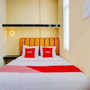 Una habitación de hotel con cama, dos almohadas con la palabra 'OYO' y una colcha estampada en rojo y blanco, y una ventana a la derecha.