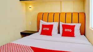 A hotel room with a bed, two pillows with 'OYO' branding, a bedside table, and a wall-mounted light. - Super OYO 93930 The Sunny Inn (Medan)