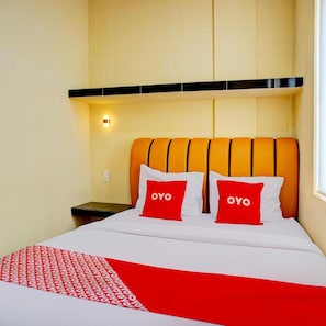 Habitación de hotel con cama, dos almohadas con la marca 'OYO', una mesita de noche y una lámpara de pared.