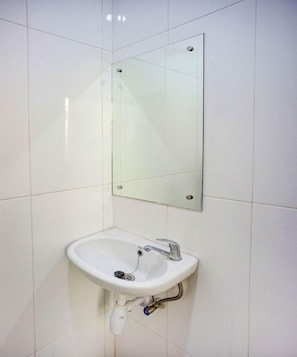 A bathroom with a white sink, a mirror, and a wall-mounted light fixture. - Super OYO 93930 The Sunny Inn (Medan)