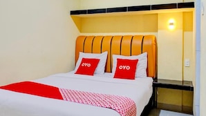 A hotel room with a bed, two pillows with the word 'OYO' on them, a red and white patterned throw, and a nightstand with a lamp. - Super OYO 93930 The Sunny Inn (Medan)