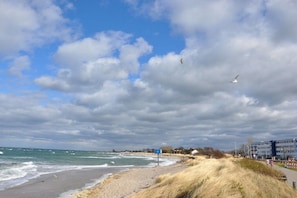Een strand met een zandstrand, golven en een gedeeltelijk bewolkte lucht.