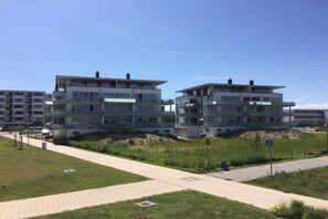 Un immeuble d’appartements moderne, doté de plusieurs étages et de balcons, situé à côté d’une promenade dallée et d’une zone herbeuse.