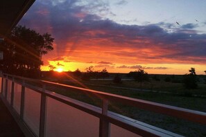 A sunset view from a balcony with a railing, trees, and a road in the foreground. - Holiday apartment with 2 bedrooms (Heiligenhafen)