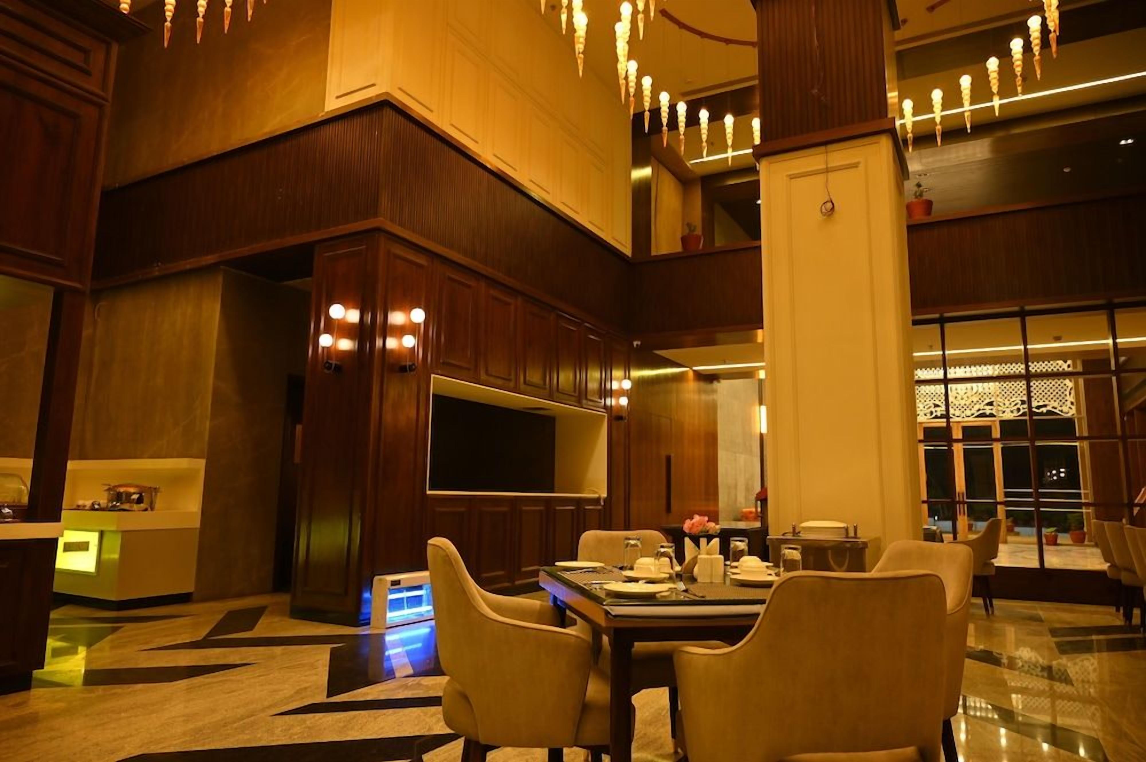 A hotel lobby with a reception desk, a dining area with chairs and a table set for two, and a large screen.