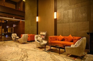 Un hall con piso de mármol, zona de estar con sillones y un sofá, y un mostrador de recepción.