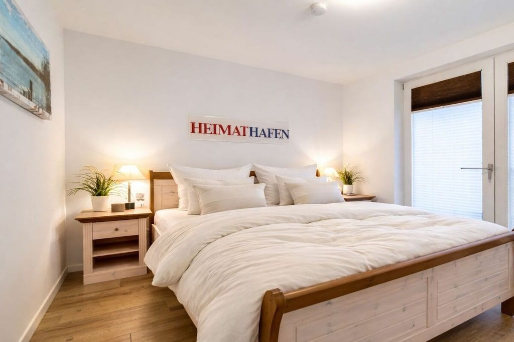 Quarto com cama, mesas de cabeceira, um letreiro fixado na parede e uma porta.