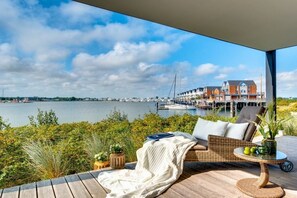 A deck with a wicker sofa, a small table, and a view of a marina with boats and buildings. - Holiday apartment with 2 bedrooms (Kappeln)