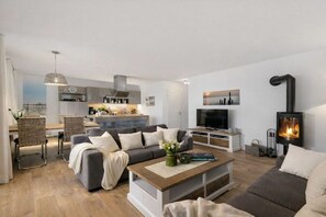 Ett modernt vardagsrum med en soffa, ett soffbord och en tv. Det finns också en köksdel med skåp och en spis.