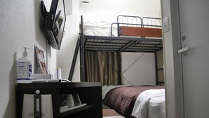 A compact hotel room with bunk beds, a desk with a chair, a small table, and a wall-mounted TV. - Hotel Glany's Kumagayaekimae (Kumagaya)