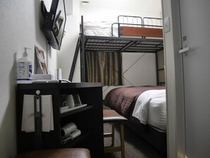 Una camera d'albergo compatta con letti a castello, una scrivania con sedia, un tavolino e una TV fissata al muro.