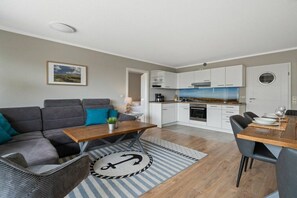 A modern living space with a sofa, dining table, and kitchen area. - Utholm 4a - Big Breeze (St. Peter-Ording)
