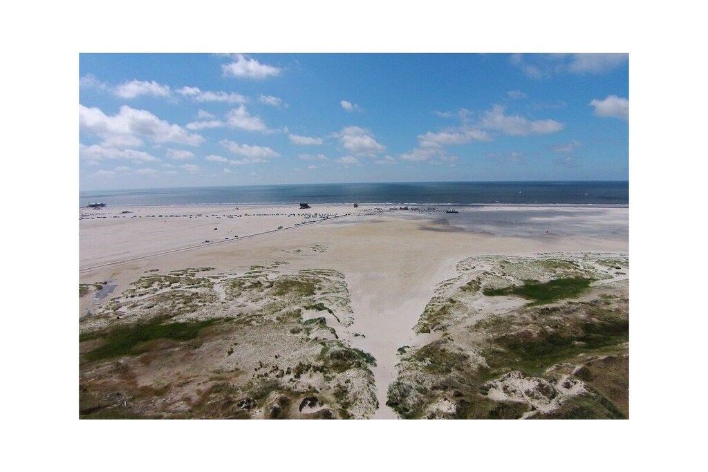 Eine Küstenlandschaft mit Sandstrand, blauem Himmel und weiter Meerblick.