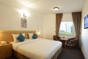 Une chambre d’hôtel comprenant un lit, une table de chevet avec un téléphone, un bureau avec une chaise, une fenêtre avec des rideaux et un téléviseur fixé au mur.