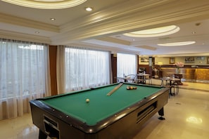 Une table de billard dans une chambre d’hôtel, avec un coin bar et des sièges.