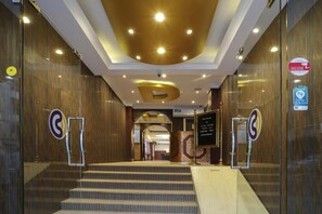 A hotel lobby with a grand staircase, a reception desk, and a large illuminated letter 'P' on the ceiling. - Click Grand Hotel LLC (Dubai)