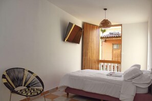 Ein Schlafzimmer mit einem Bett, einem Sessel, einem an der Wand befestigten Fernseher und einer Holztür, die zu einem Außenbereich führt.