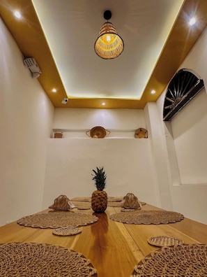 A dining area with a wooden table, woven placemats, a pineapple centerpiece, and a hanging light fixture. - Hostal Casa Torres Centro Historico Adults Only (Cartagena)