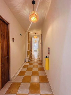 A hotel corridor with checkered flooring, a wooden door, a fire extinguisher, and hanging pendant lights. - Hostal Casa Torres Centro Historico Adults Only (Cartagena)
