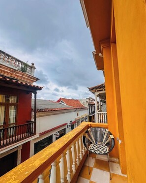 A balcony with a yellow railing, a patterned chair, and a view of neighboring buildings with red-tiled roofs. - Hostal Casa Torres Centro Historico Adults Only (Cartagena)