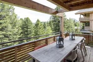 Eine Holzterrasse mit Tisch und Stühlen, mit Blick auf eine bewaldete Landschaft.