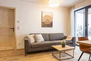 A modern living room with a grey sofa, a wooden coffee table, and a painting of a mountain on the wall. - Holiday apartment & infinity pool (St. Martin am Tennengebirge)