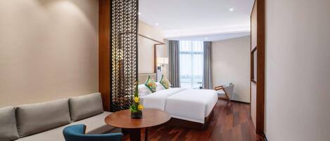 A hotel room with a sofa, a bed, a small table with flowers, and a decorative screen.