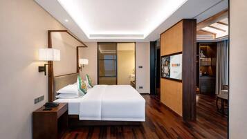A modern hotel room with a large bed, bedside lamps, a wooden floor, and a view into the adjacent room.