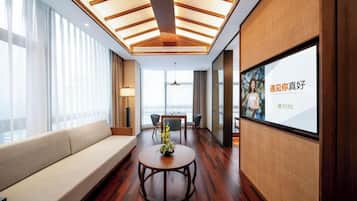 A modern hotel room with a wooden ceiling, a sofa, a round table with a vase, and a large window.
