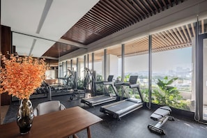 A modern gym with treadmills, exercise equipment, and large windows offering a city view.