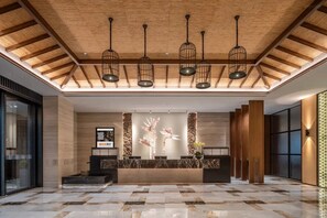 Vestíbulo de hotel con mostrador de recepción, vigas de madera en el techo y lámparas colgantes.