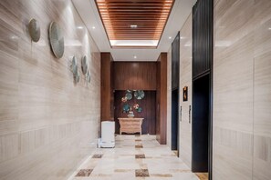 Un hall d’entrée moderne avec un sol en marbre, un plafond recouvert de panneaux en bois et un comptoir d’accueil agrémenté d’objets décoratifs.
