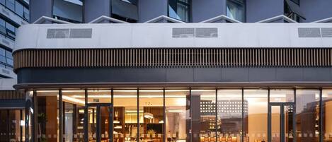 A modern building with a glass facade, outdoor seating area, and a visible entrance.